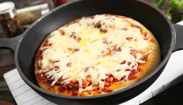Pizza caseira derretendo na frigideira com queijo derretido e molho visível.