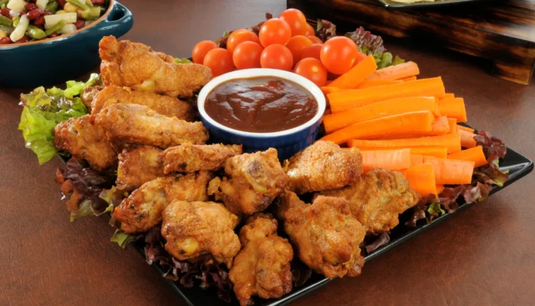 Prato de petiscos com asas de frango empanadas, molho barbecue, cenoura, tomates cereja e salada.