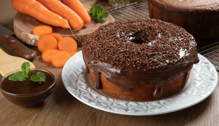 Bolo de cenoura com cobertura de chocolate e granulado, acompanhado de cenouras frescas.