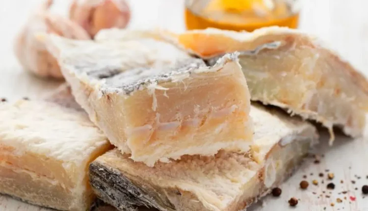 Imagem de bacalhau dessalgado, pronto para ser preparado na Páscoa, com alho e especiarias ao fundo.