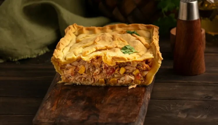 Torta portuguesa de liquidificador com recheio de frango, milho e tomate, servida em uma tábua rústica de madeira.