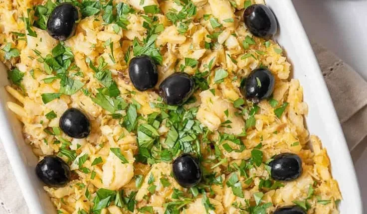 Prato de bacalhau com batatas, azeitonas pretas e ervas frescas, típico da culinária de Páscoa.