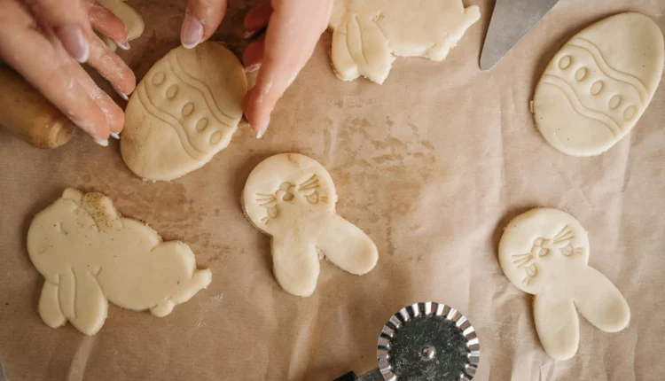 Mãos moldando biscoitos temáticos de Páscoa em formatos de coelho e ovo.