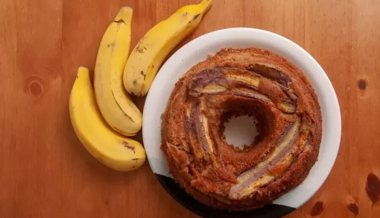 Bolo de banana light decorado com fatias da fruta, servido em prato branco sobre mesa de madeira