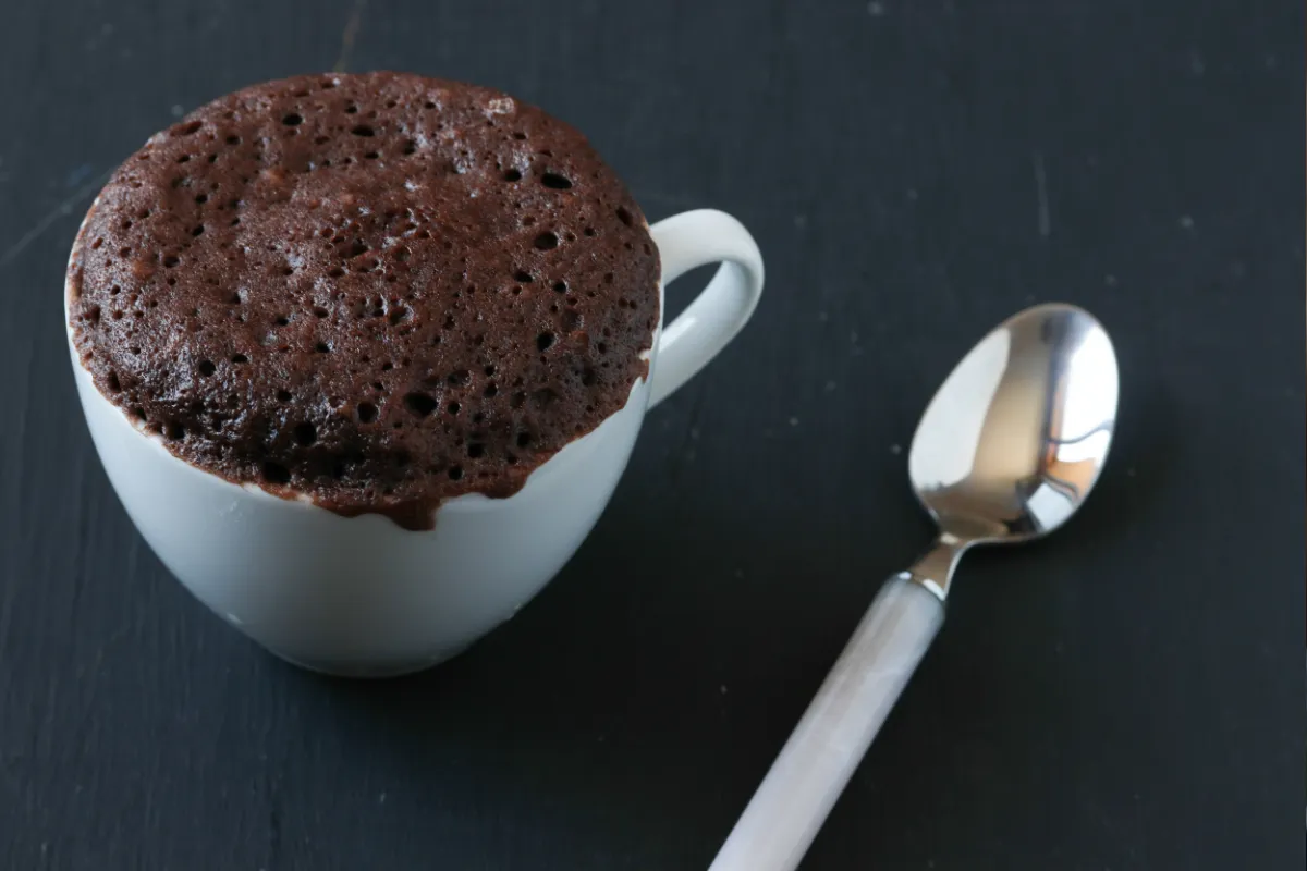 Bolo de caneca feito no micro-ondas Bolo de caneca de chocolate com uma colher ao lado.