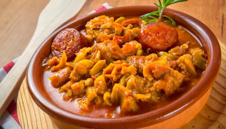 Prato de dobradinha com linguiça e legumes em uma tigela de barro.