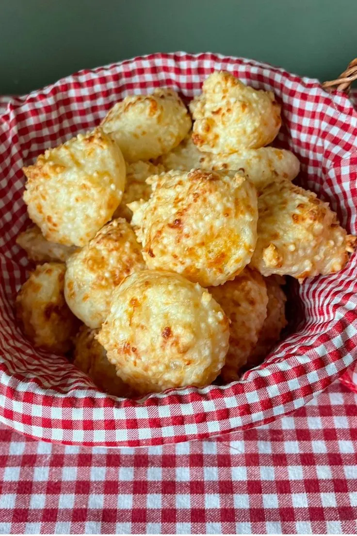 Modelagem dos pãezinhos de tapioca Bolinhas de pão de tapioca modeladas em cesto com pano xadrez vermelho.