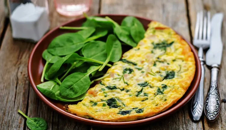 Omelete verde com espinafre no prato, acompanhado de folhas frescas