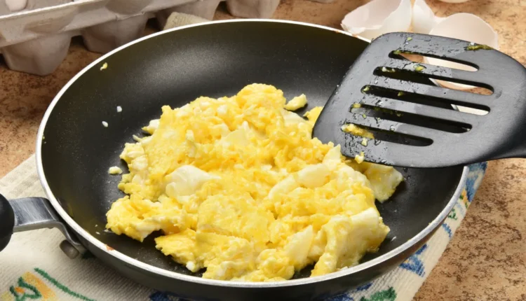 Ovos mexidos recém-preparados em uma frigideira com espátula plástica preta.