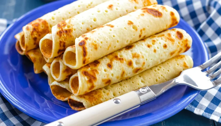 Panquecas enroladas em cima de um prato azul com um garfo ao lado.