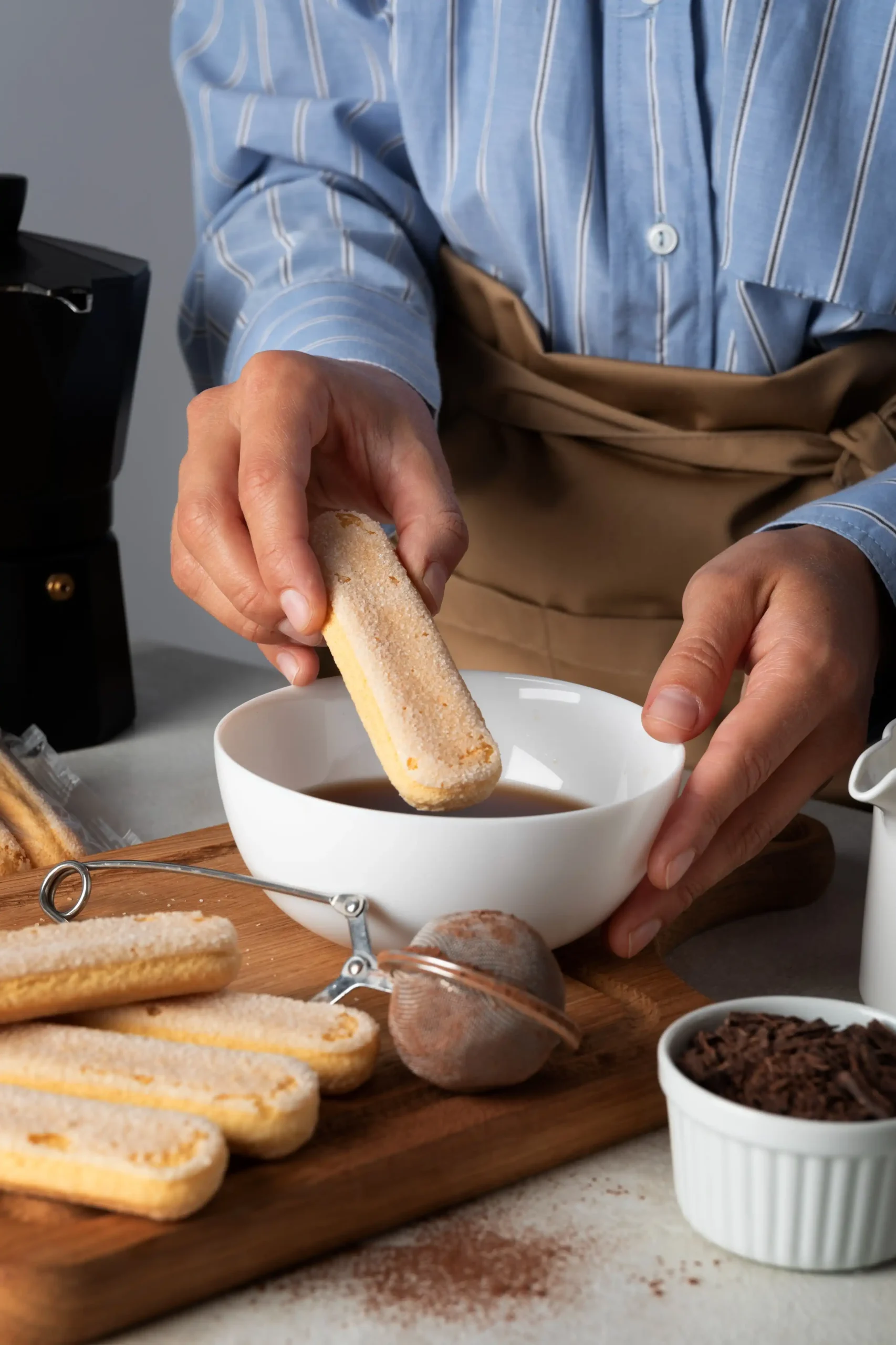 Pessoa mergulhando biscoito ladyfinger em café para preparar tiramisù.