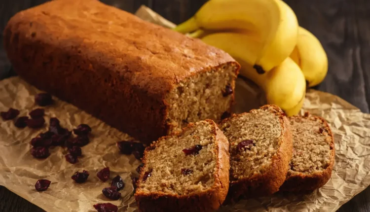 Bolo de Banana com Cranberries Bolo de banana com cranberries, cortado em fatias, servido com bananas frescas ao fundo