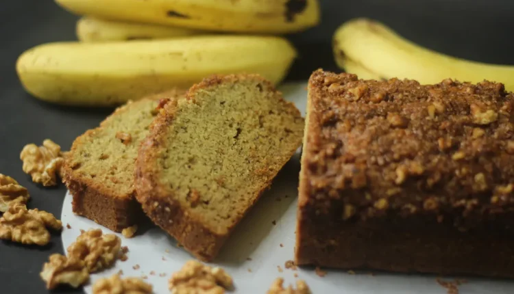 Bolo de banana com farinha de rosca e nozes, cortado em fatias, servido com bananas frescas ao fundo