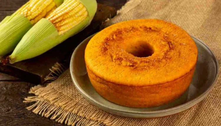 Bolo de milho caseiro com textura macia servido em prato rústico, ao lado de espigas de milho frescas.