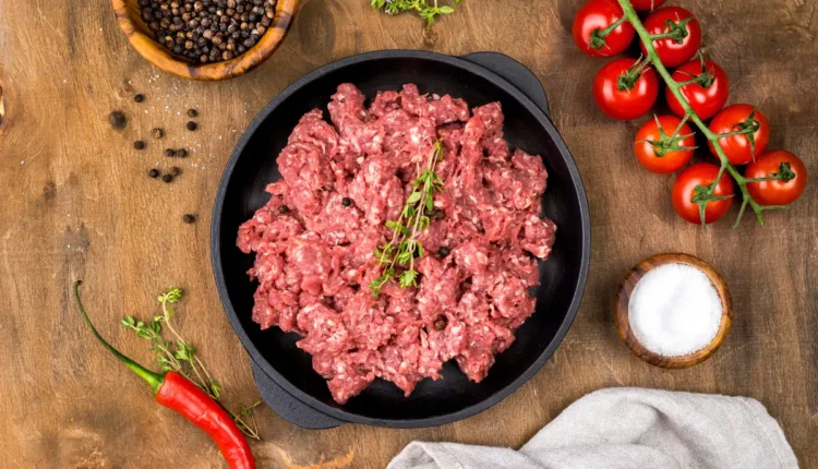 Carne moída fresca em frigideira preta com temperos e tomates ao redor.