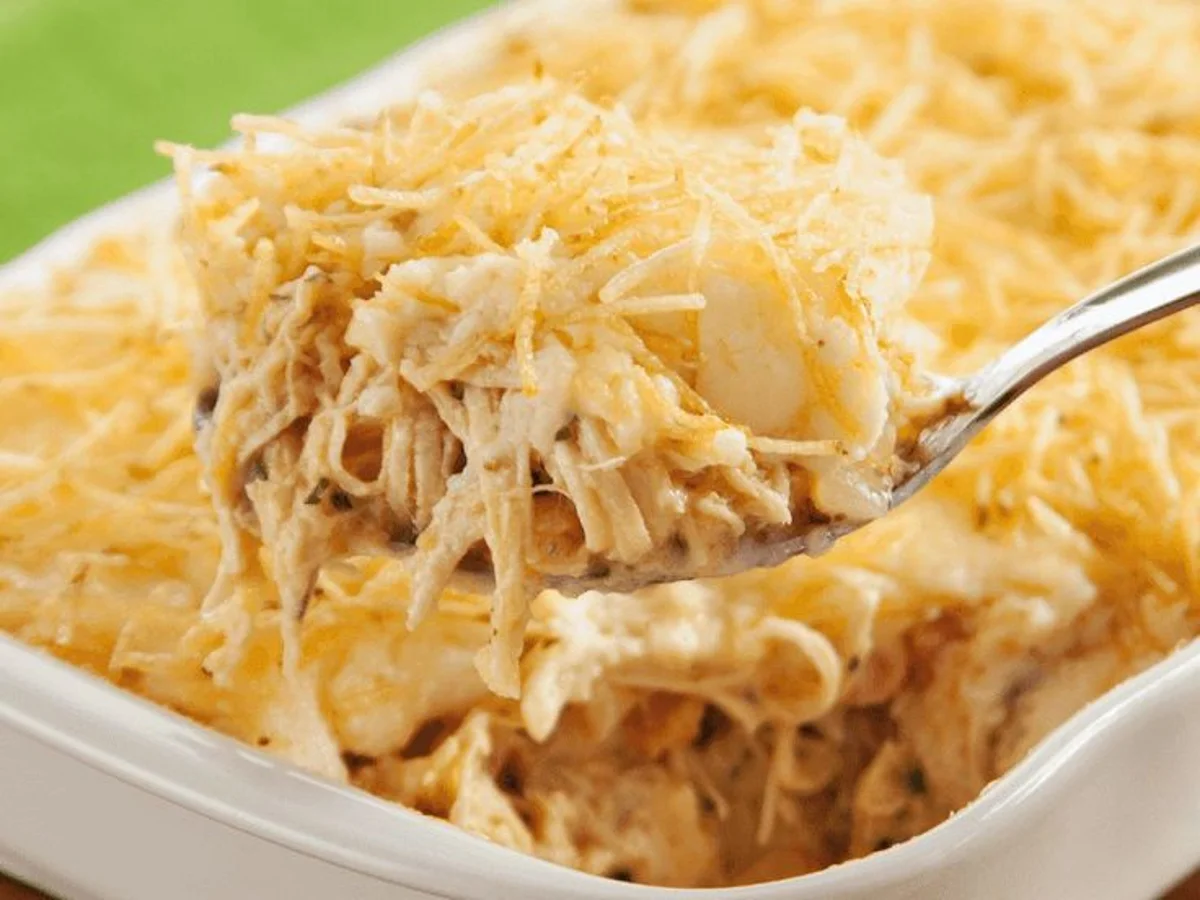 Fricassê de Frango Cremoso Servido Prato de fricassê de frango cremoso sendo servido com batata palha crocante.
