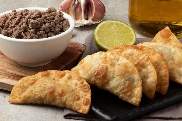 Pastel de carne moída dourado e saboroso Pastel crocante recheado com carne moída bem temperada, acompanhado de limão e alho.