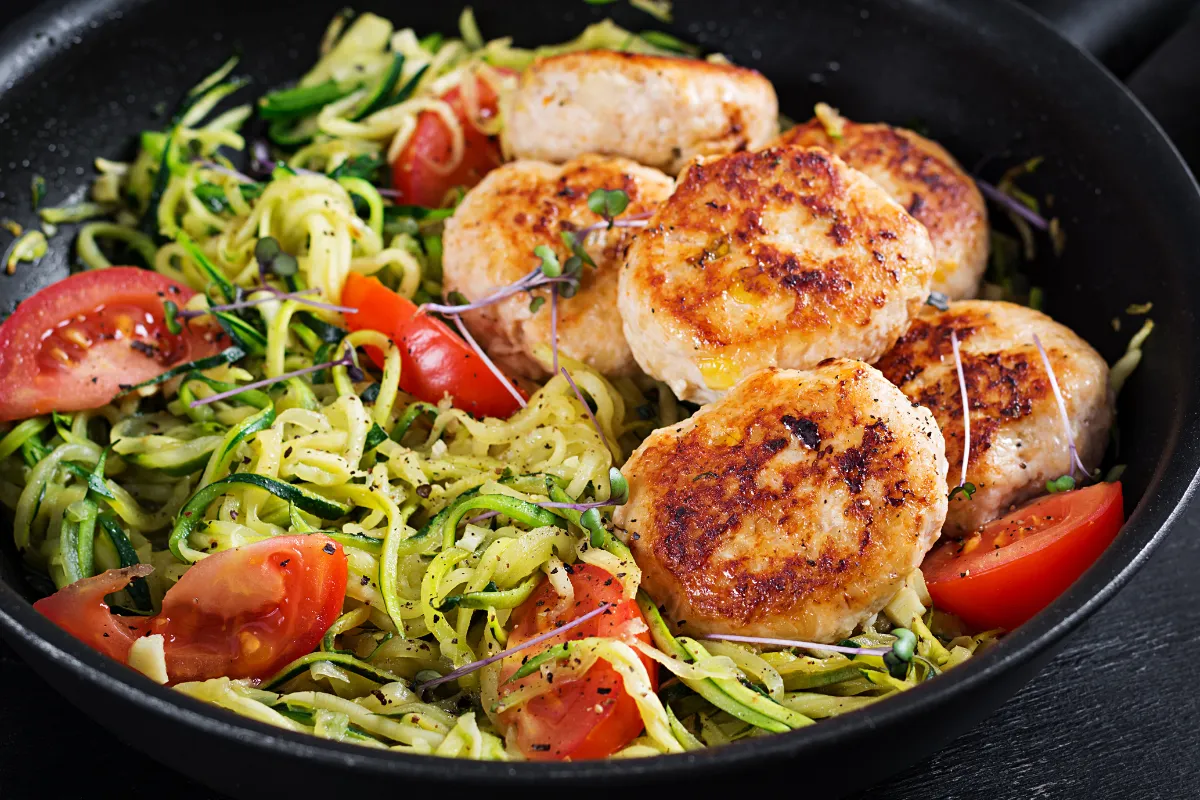 Frango grelhado com abobrinha espiralizada e tomate Frango grelhado servido com abobrinha espiralizada e tomate fresco em uma panela.