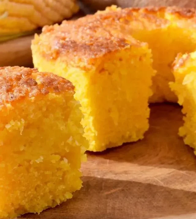 Bolo de Milho Cremoso Cortado em Fatias. Fatias de bolo de milho cremoso com textura macia e dourada, servidas em uma tábua de madeira.
