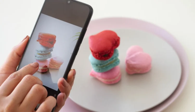 Mãos fotografando macarons em forma de coração com o celular.