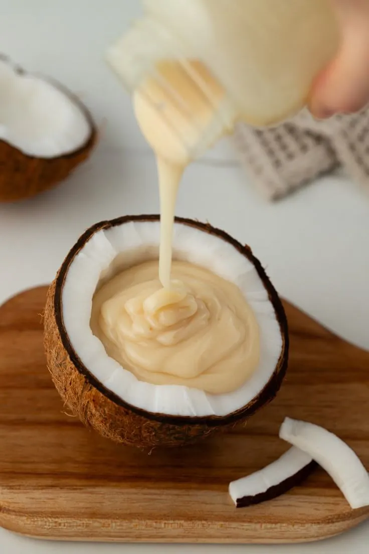 Leite condensado de coco servido em fruta natural Leite condensado vegano sendo despejado em meio coco fresco.