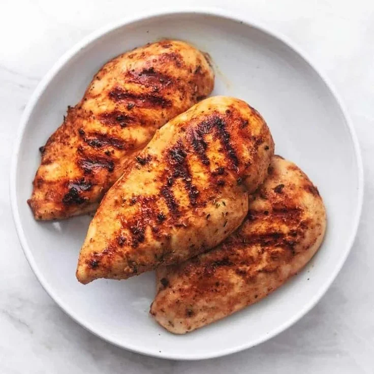 Peito de frango grelhado dourado e suculento Peitos de frango grelhados, dourados e suculentos, servidos em um prato branco.
