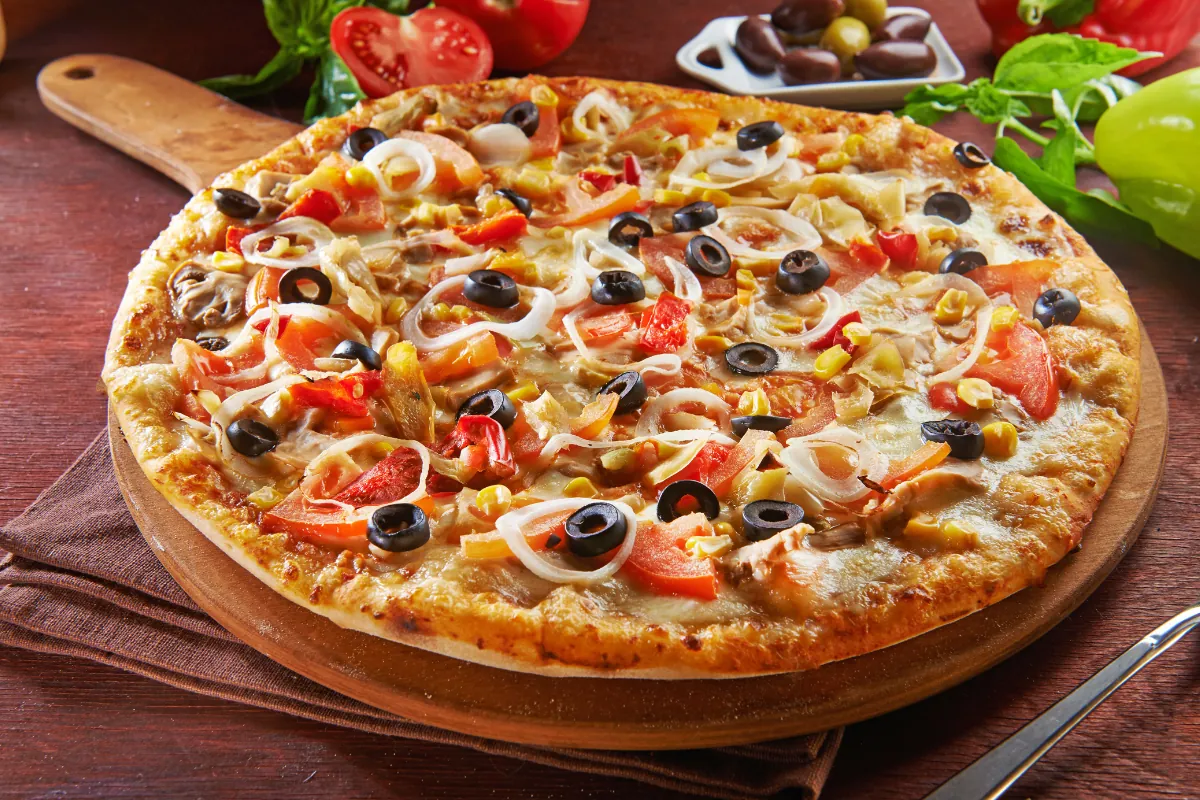 Pizza caseira saborosa e colorida Pizza caseira com queijo, azeitonas, cebola, pimentão e milho, recém-assada sobre uma tábua de madeira.