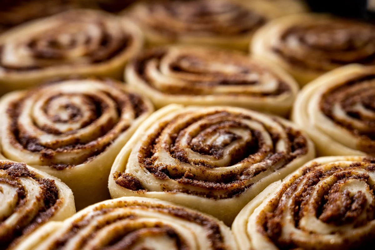 Rolo de canela vegano Rolinhos de canela frescos, enrolados e prontos para assar, com uma camada de açúcar e canela visível.