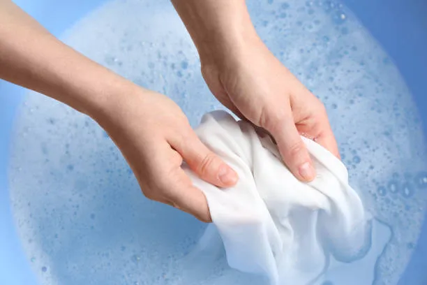 Mulher lavando roupa manchada com sabonete branco em uma bacia azul