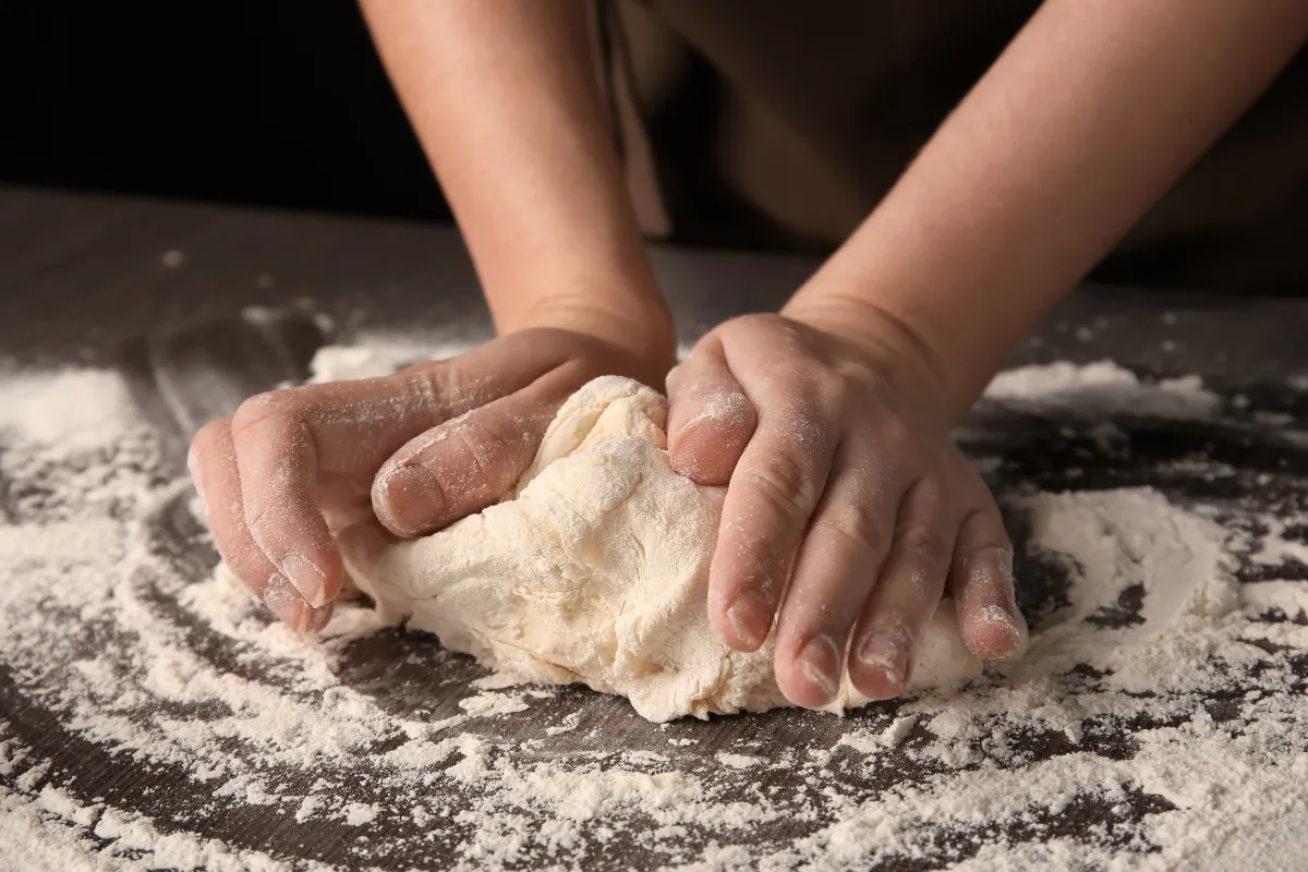 Sovando massa de pizza artesanal Mãos sovando massa de pizza sobre uma superfície enfarinhada.