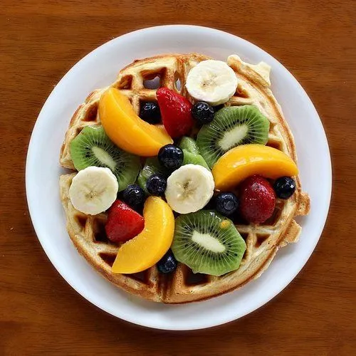 Waffle com Frutas - Uma sobremesa deliciosa e saudável Waffle com frutas frescas - Bananas, morangos, kiwi e manga sobre um waffle crocante.