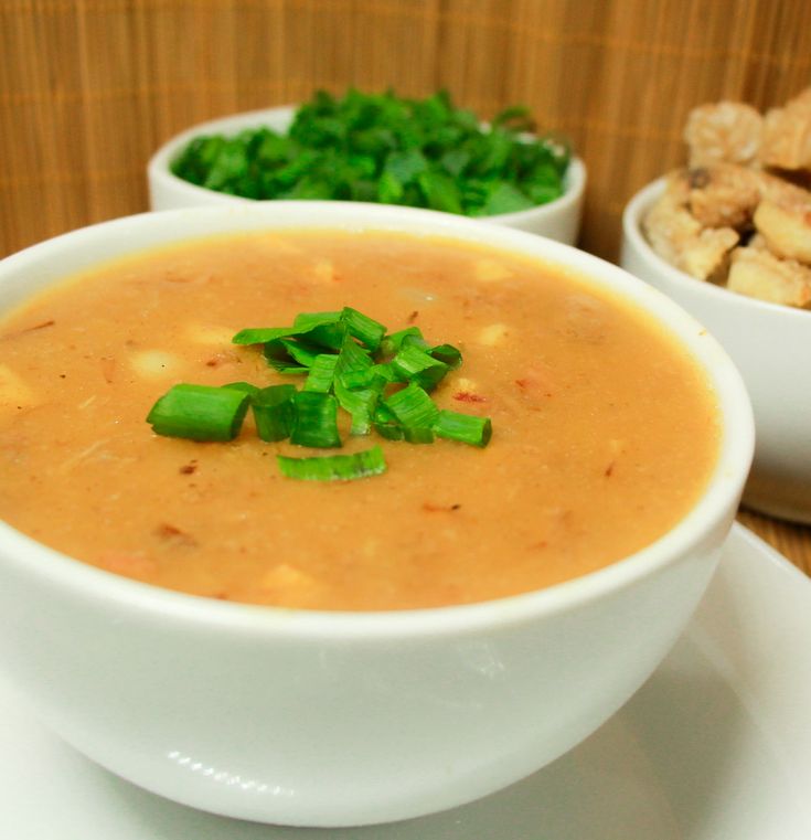 Sopa de mandioca com pedaços de carne e cebolinha picada, servida em uma tigela branca.