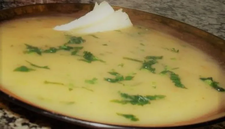 Sopa cremosa de mandioca com coentro e pedaços de queijo coalho, servida em um prato de barro.