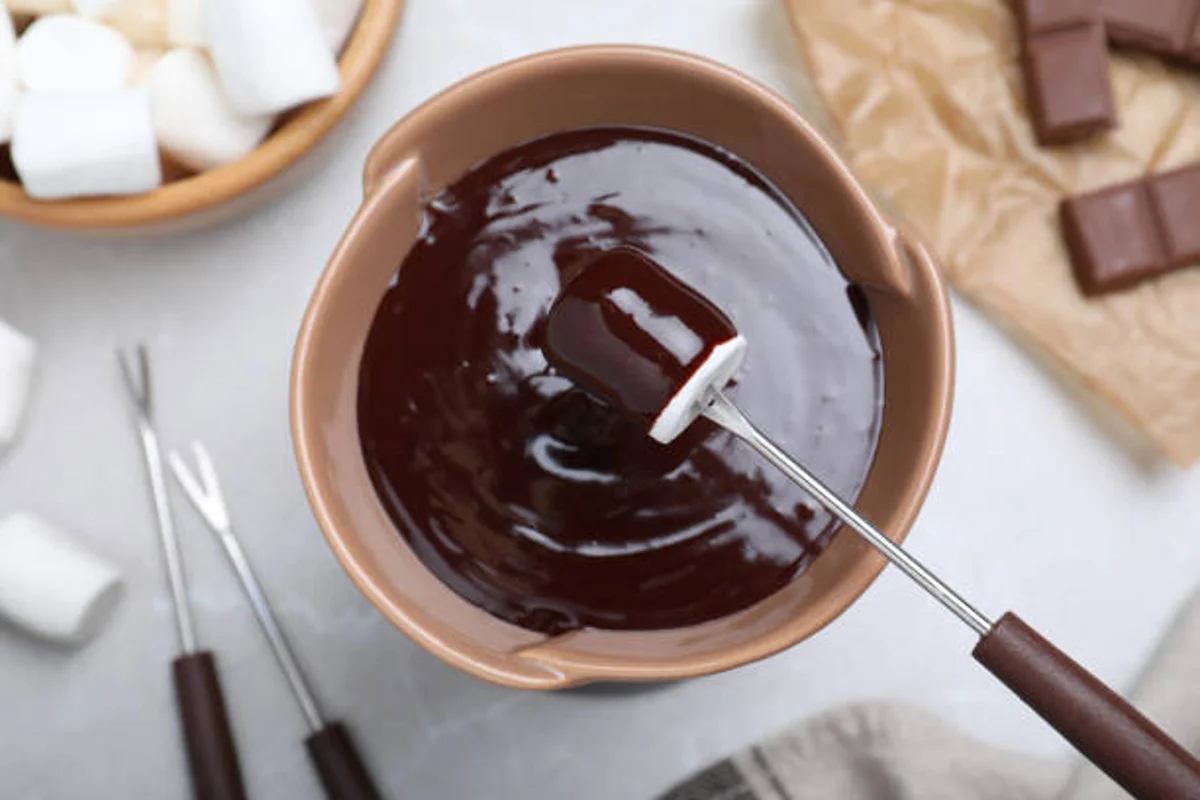 Fondue de Chocolate – A sobremesa perfeita para o Dia Mundial do Chocolate Fondue de chocolate com marshmallow sendo mergulhado